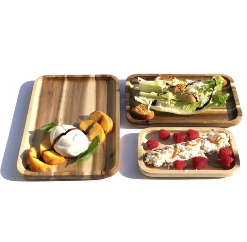 Three nesting rectangle acacia wood serving platters displaying a caprese salad, caesar salad, and raspberries with cheese.