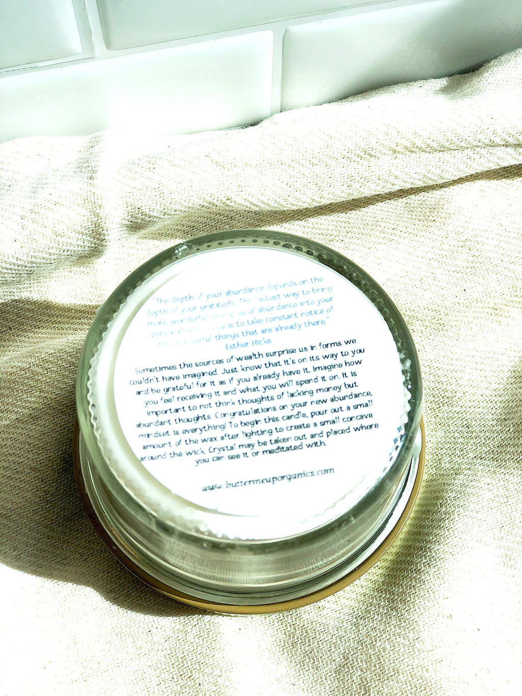 Bottom label of a clear glass abundance ritual candle showing manifestation instructions and a quote by Esther Hicks, placed on a kitchen textile.