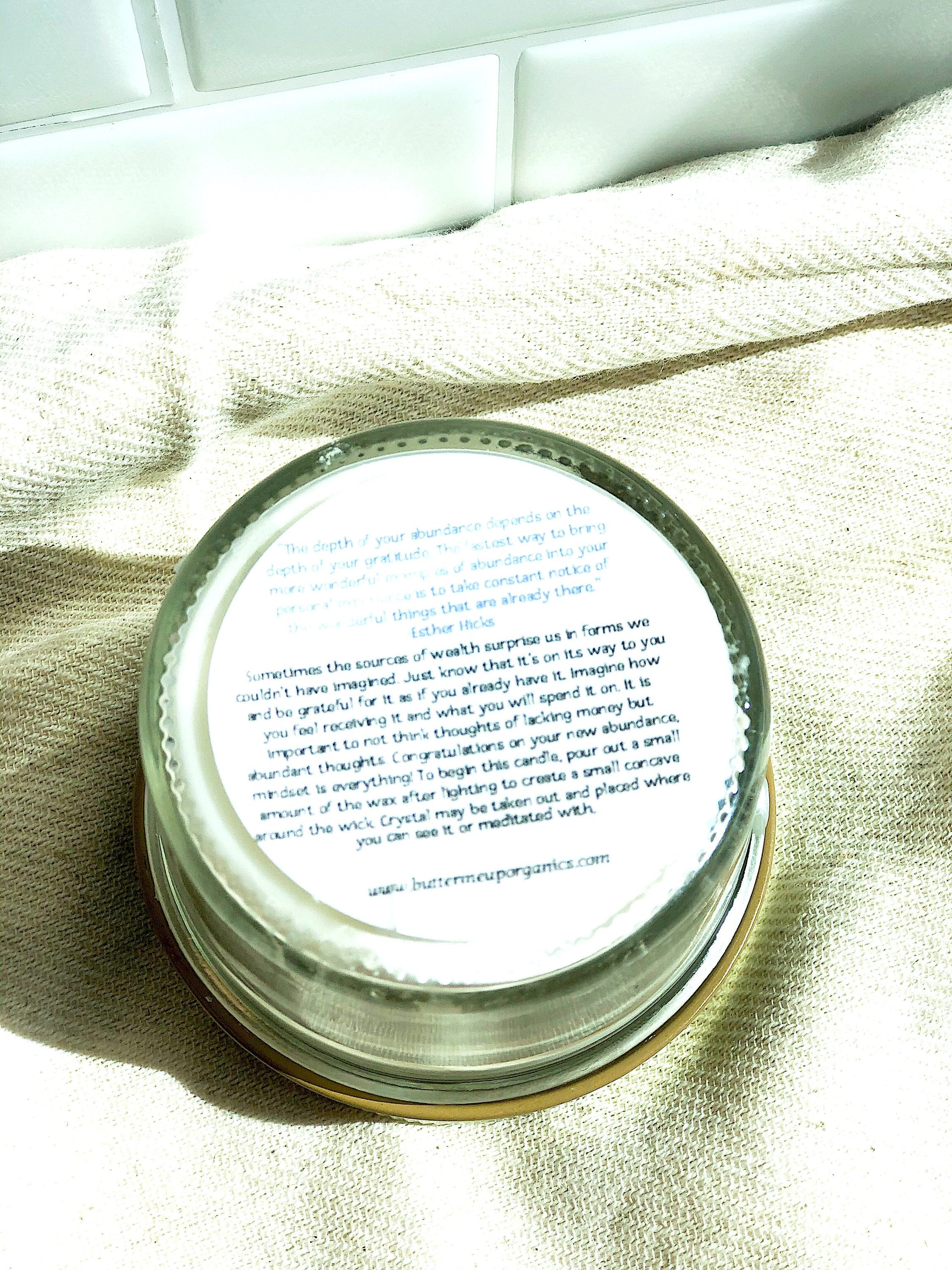 Bottom label of a clear glass abundance ritual candle showing manifestation instructions and a quote by Esther Hicks, placed on a kitchen textile.