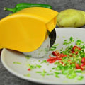 Lemon yellow rolling herb cutter mincing green and red chili peppers on a white ceramic plate.