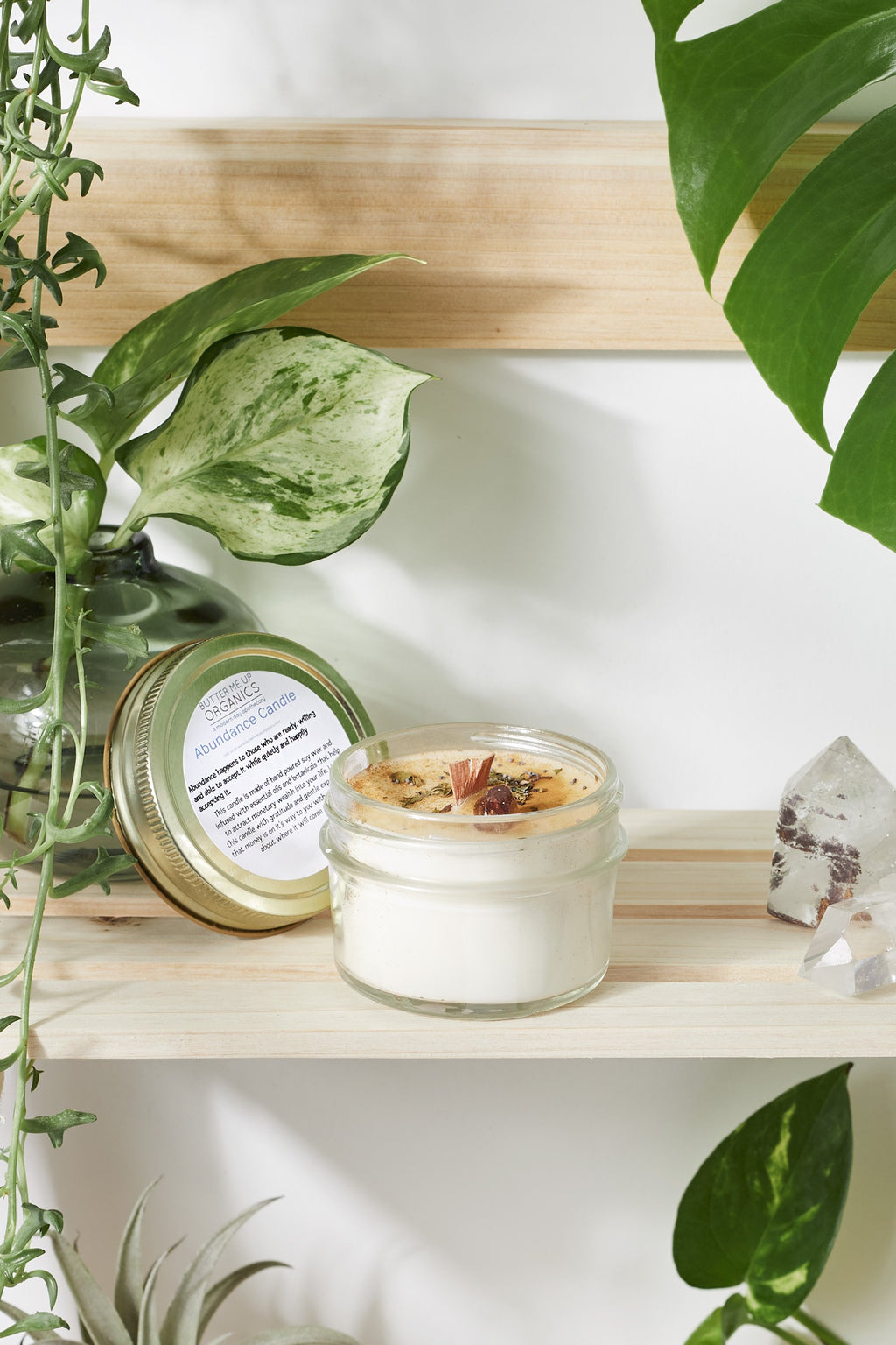 Close-up of an open soy abundance candle showing a wooden wick, dried botanicals, and a citrine crystal embedded in the wax, displayed on a wooden shelf.